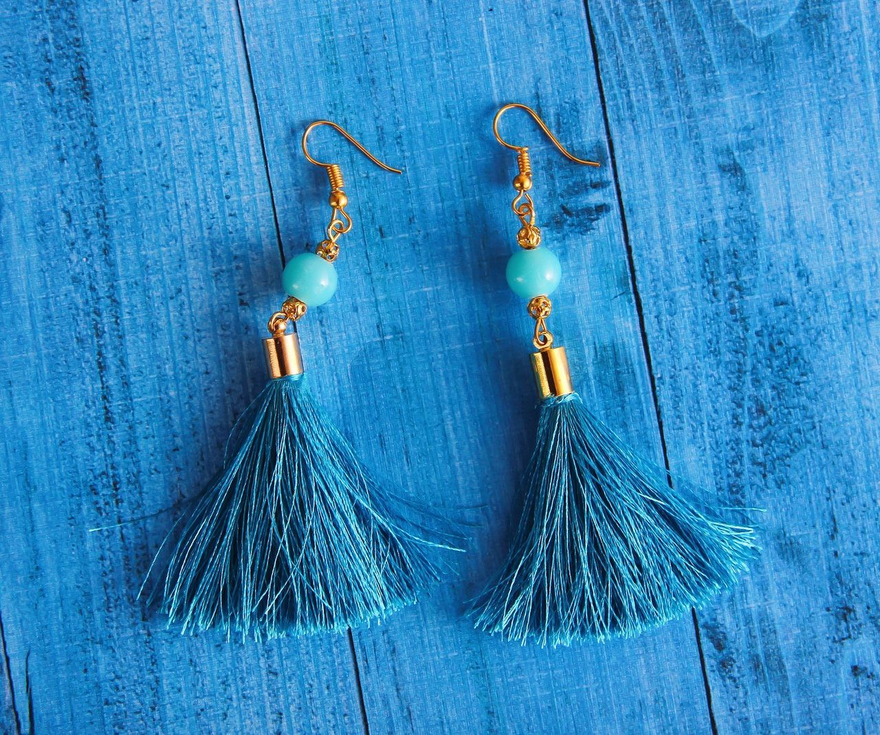 14k gold dangly earrings with a light blue bead and dark blue tassels on a blue piece of wood