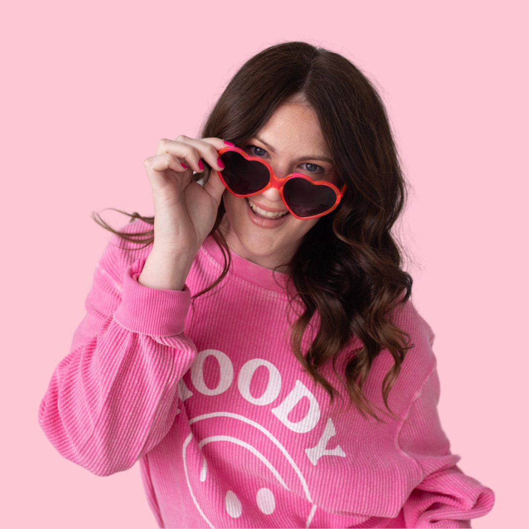 Woman wearing pink shirt and holding pink sunglasses to face