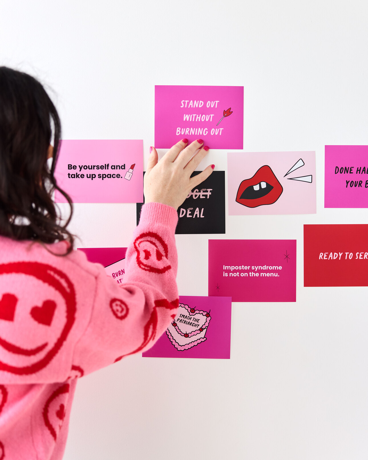Woman in pink and red sweater pinning pink and red cards to a wall